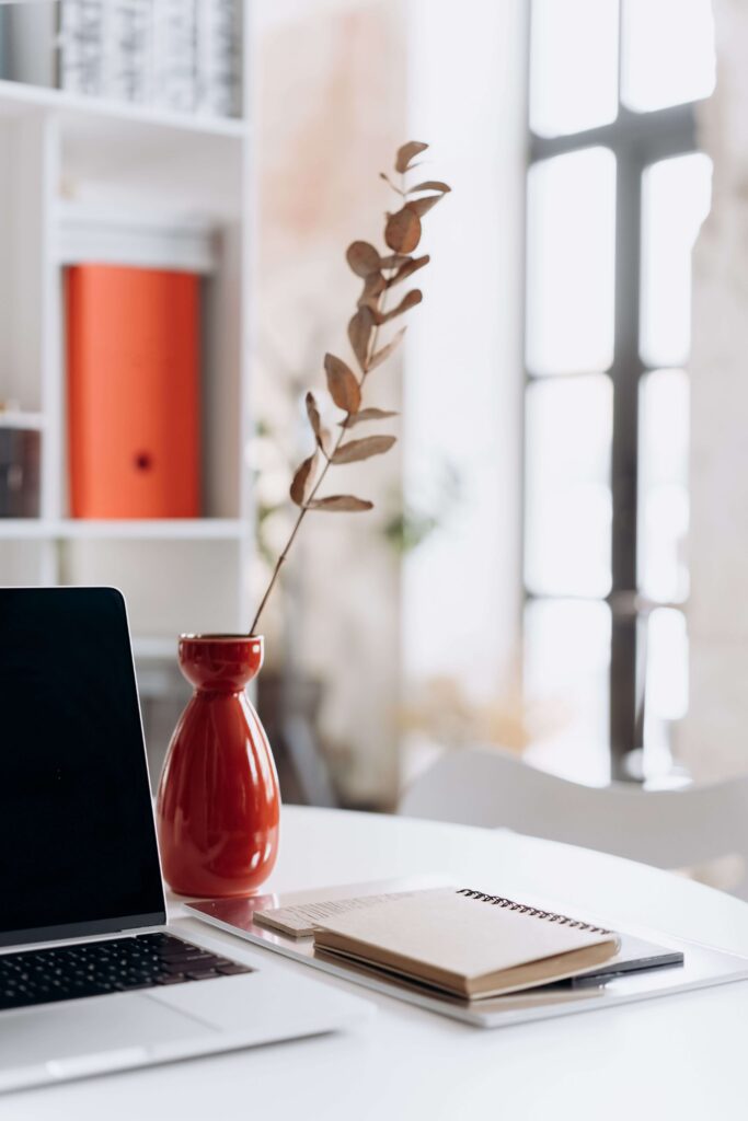Bureau organisé avec ordinateur portable, carnet de notes et vase rouge